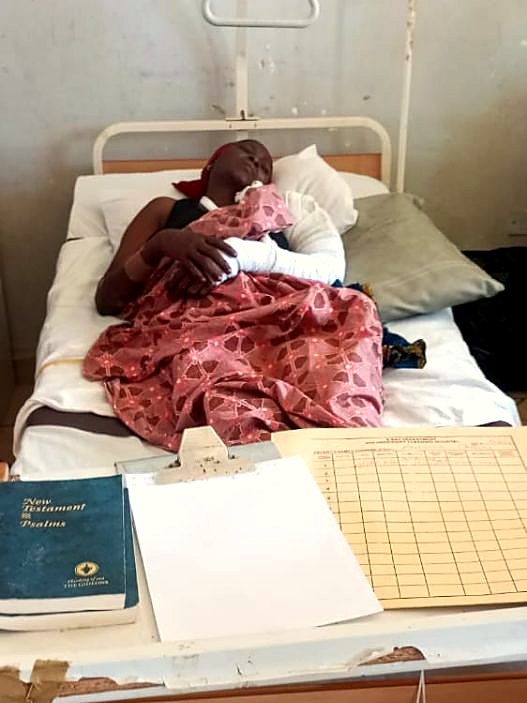 A mother recovering in a hospital bed with her arm bandaged, holding her infant